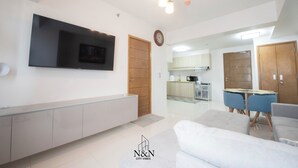 A modern living room with a flat-screen TV, a dining area with a table and chairs, and a kitchen in the background. - Relax & unwind in this 1 BR/1 Bath Condo walking distance from Ayala Mall (Cebu City)