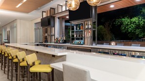 A bar area with a long counter, multiple stools, and a well-lit bar stocked with bottles. - Hilton Garden Inn Walnut Creek (Walnut Creek)