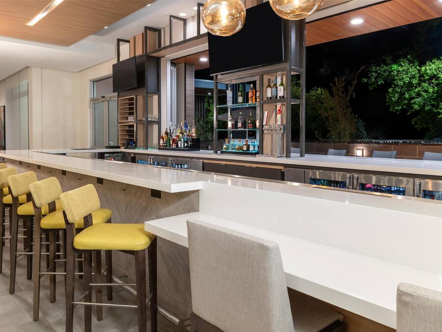 Eine Bar mit einer langen Theke, mehreren Hockern und einer gut beleuchteten Bar, die mit Flaschen bestückt ist.