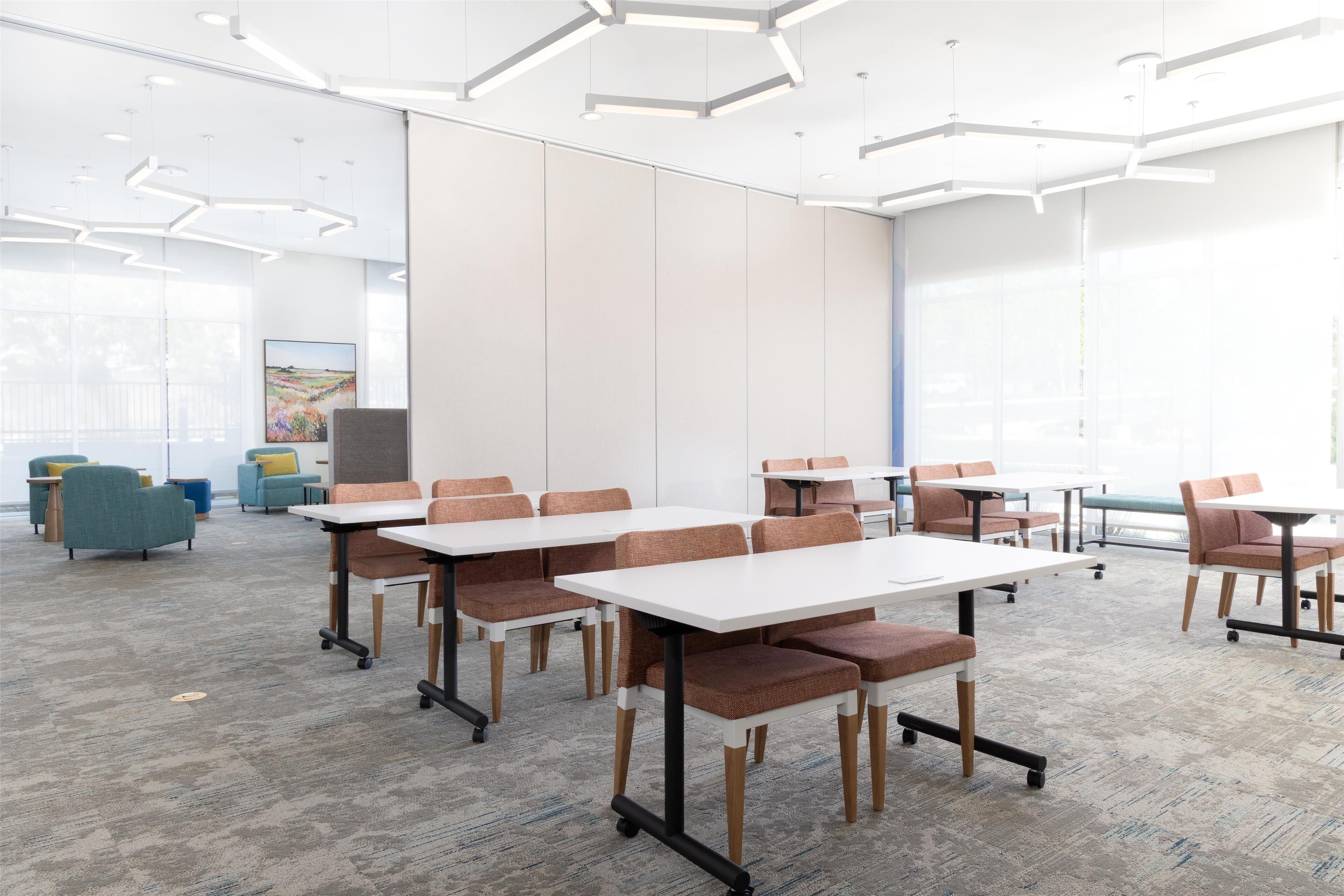 A conference room with white tables and chairs, carpeted floor, and large windows.