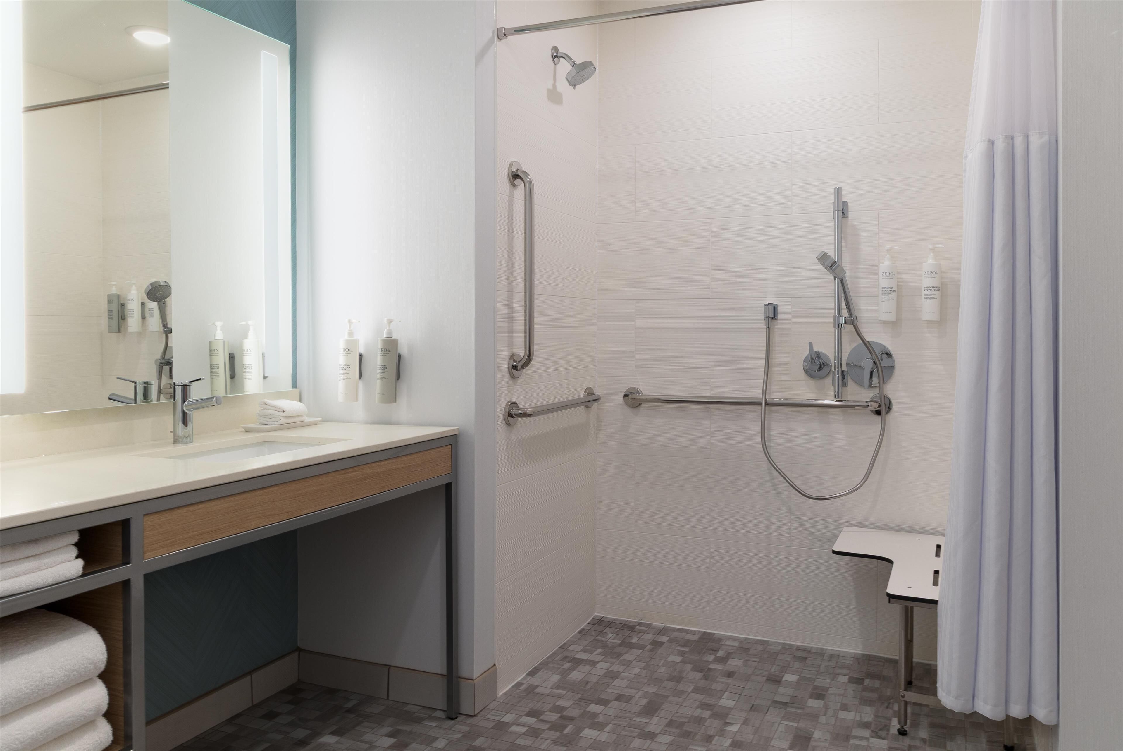 A modern bathroom with a shower, grab bars, a sink, and a mirror.