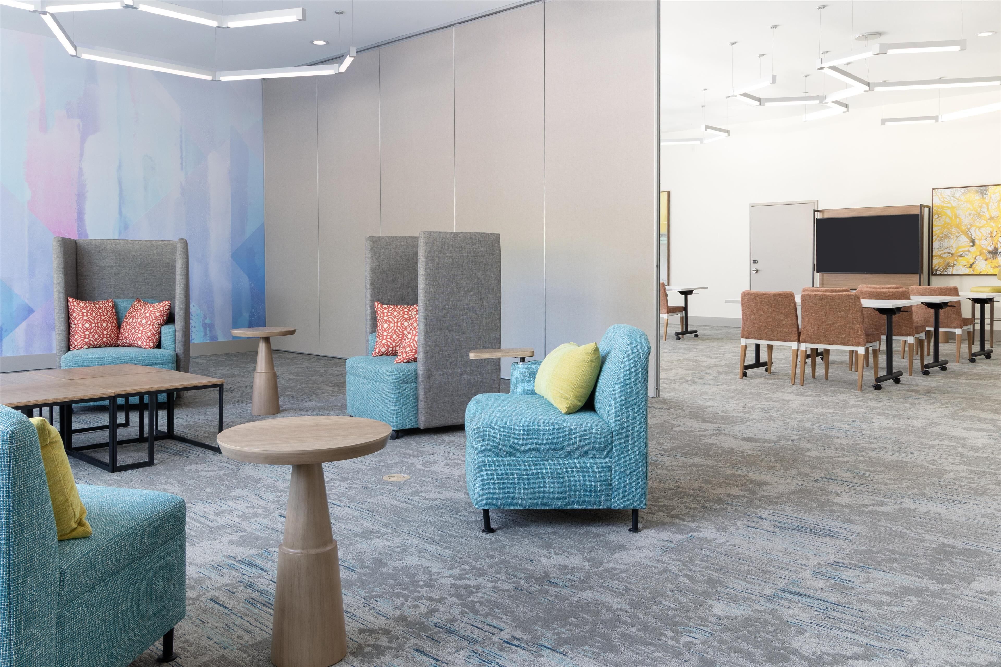 Een moderne lounge met zitplaatsen, tafels en een groot abstract schilderij aan de muur.