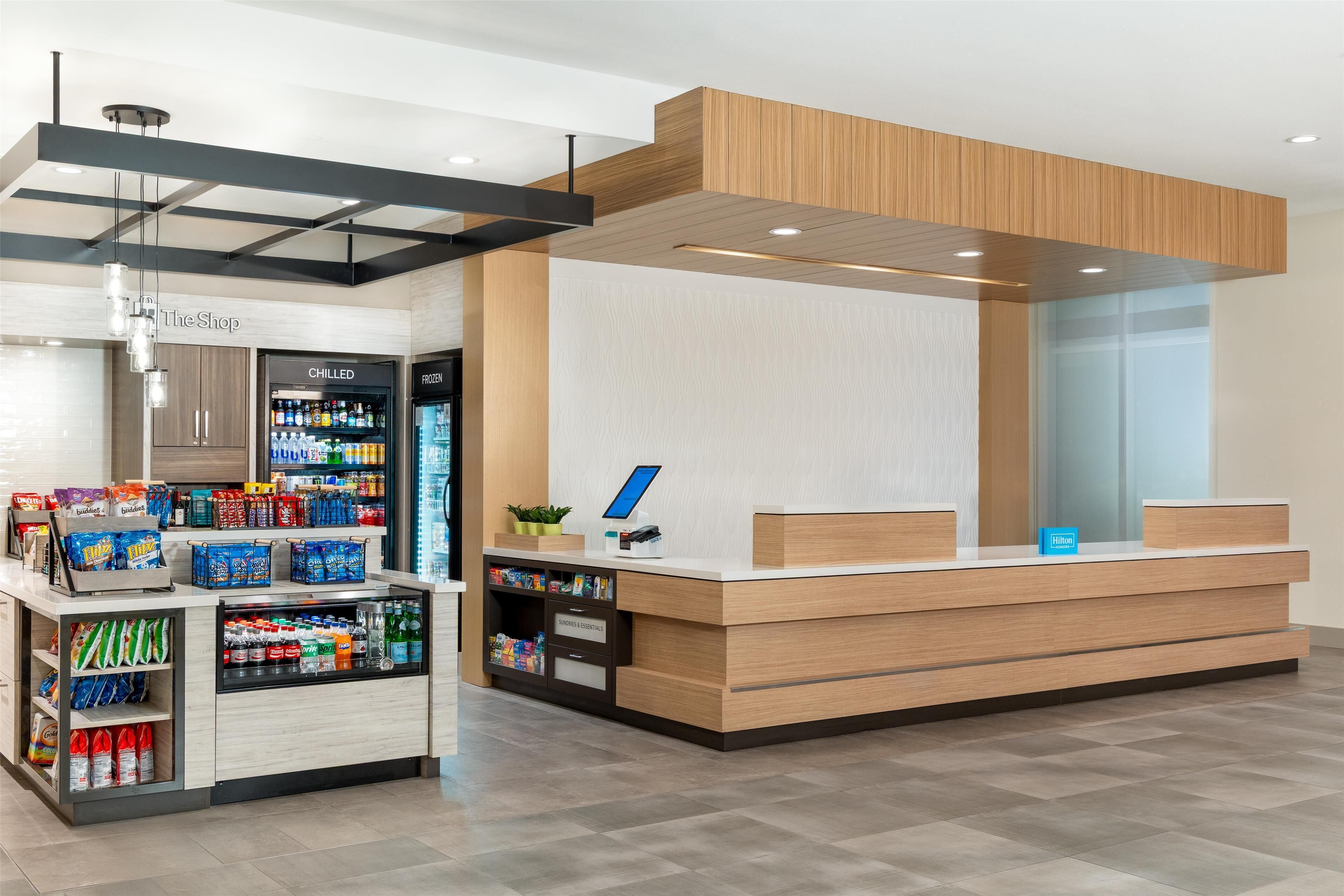 A modern reception desk with a digital screen, a chilled and frozen beverage display, and a variety of snacks and beverages.