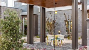 An outdoor seating area with a wooden pergola, a hanging light fixture, and a table with chairs. - Hilton Garden Inn Walnut Creek (Walnut Creek)