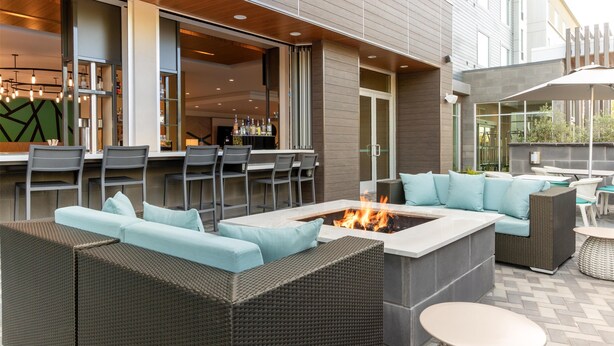 An outdoor seating area with a fire pit, wicker furniture, and a bar with stools. - Hilton Garden Inn Walnut Creek (Walnut Creek)