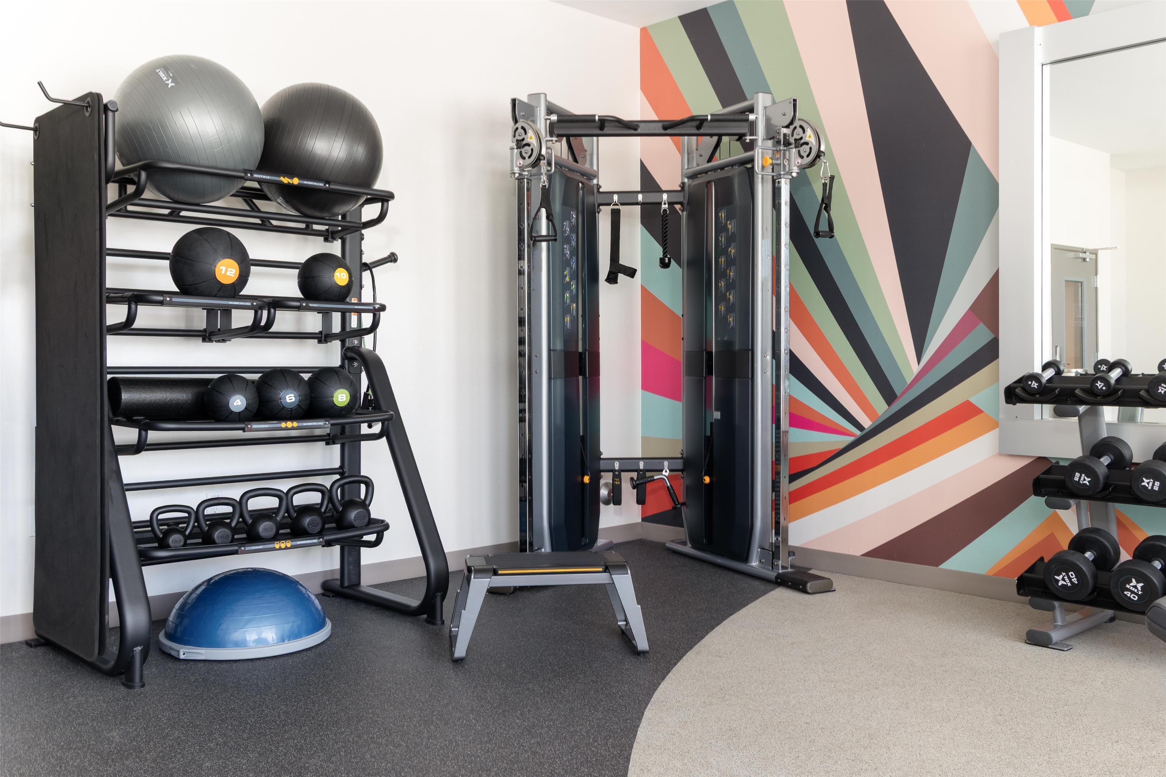 Une salle de sport équipée de divers appareils, notamment un support à squats, des balles lestées, des kettlebells et des haltères.