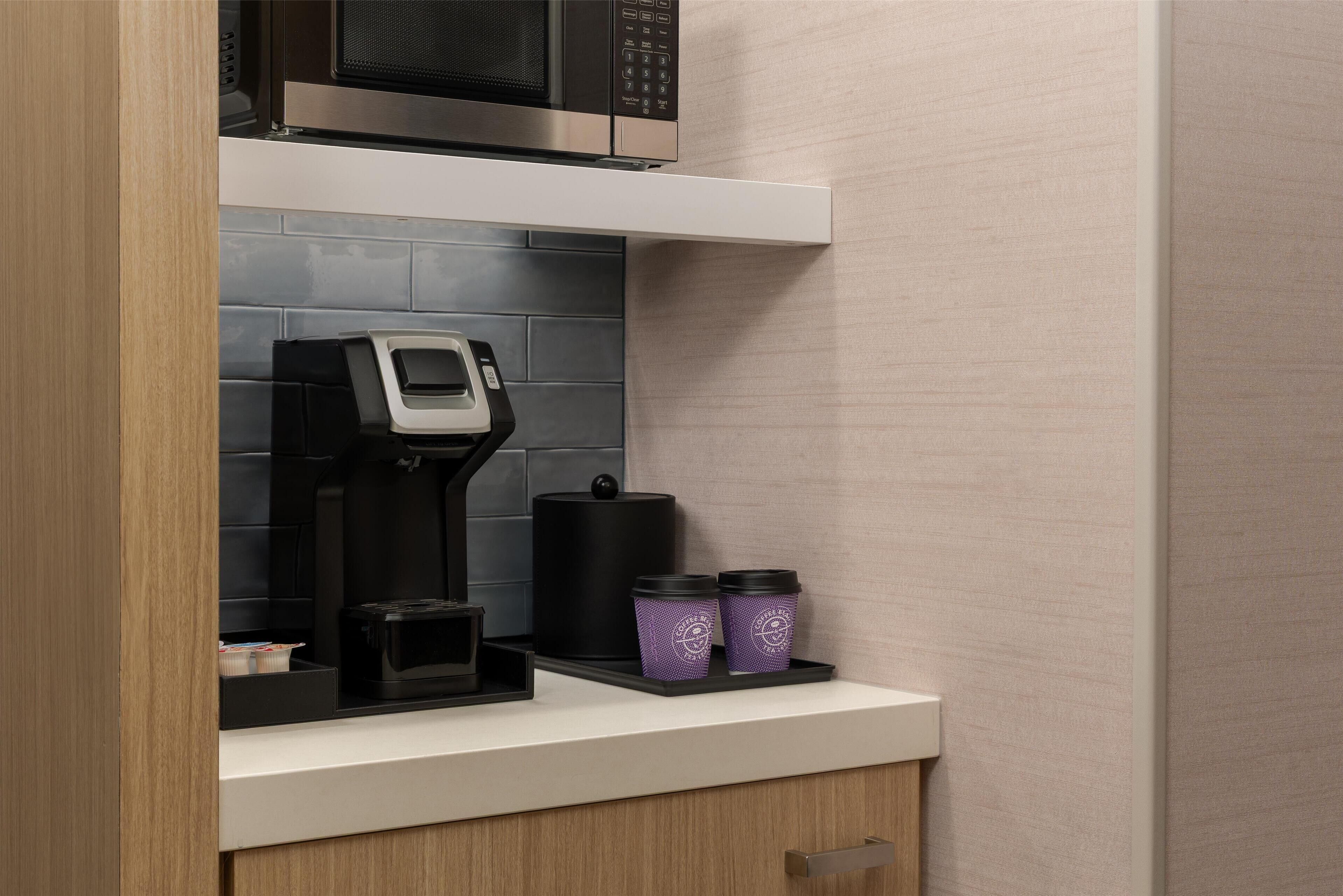 Una cocina con cafetera, microondas y dos recipientes morados en la encimera.