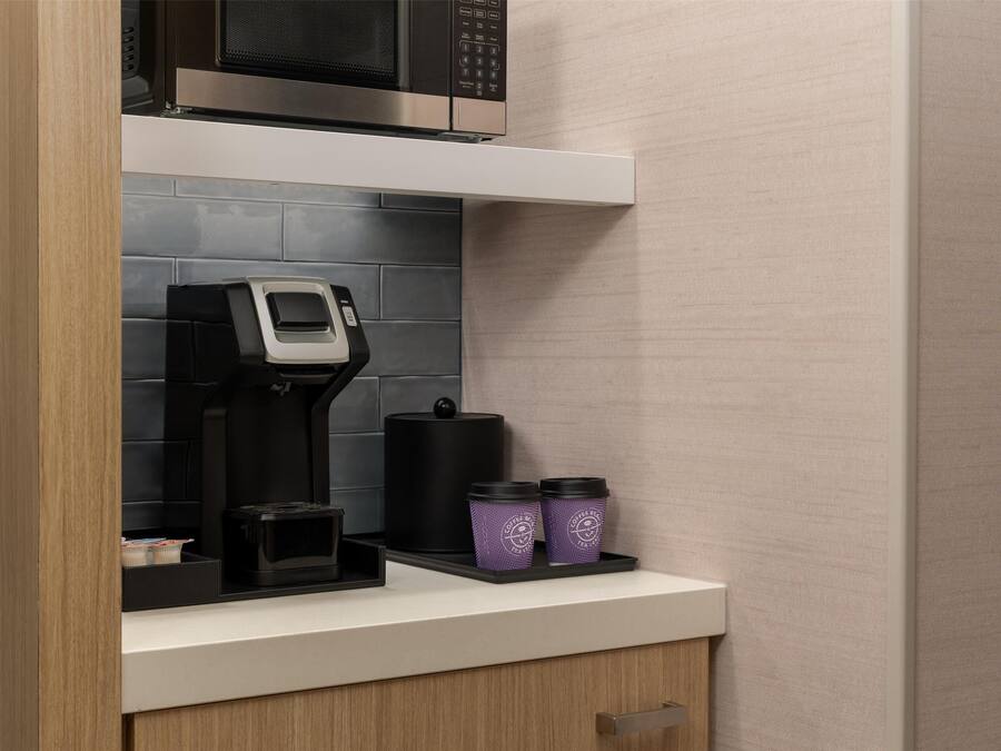 Una cocina con cafetera, microondas y dos recipientes morados en la encimera.