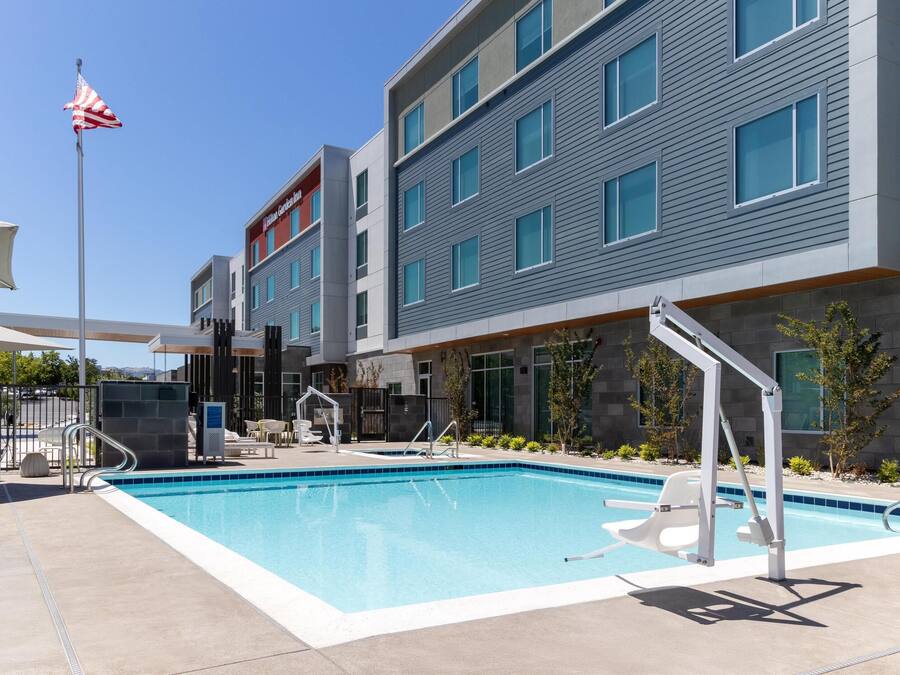 A modern hotel with a swimming pool, outdoor seating, and a flagpole.