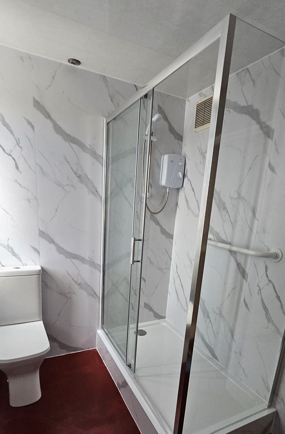 A bathroom with a glass-enclosed shower, a white toilet, and marble walls.