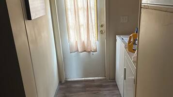 A narrow hallway with a door at the end, a small cabinet with a bottle of detergent, and a sign on the wall.