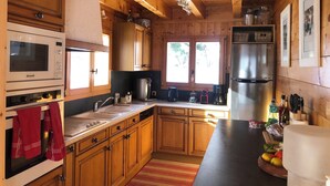 Cocina de cabaña de madera con horno Brandt, refrigerador de acero inoxidable y armarios de madera.