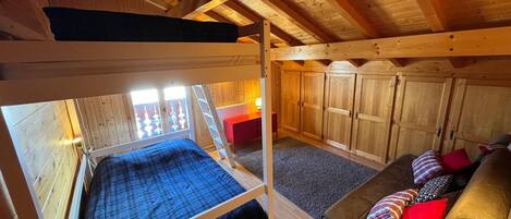 Dormitorio con literas, techo de madera, escritorio rojo y sofá marrón con almohadas.