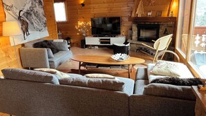 Acogedor interior de cabaña de madera con una sala de estar moderna, una chimenea y un televisor grande.
