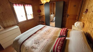Un dormitorio de cabaña de madera con una cama, un espejo, un armario y una ventana con cortinas.