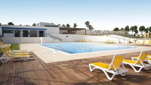 Piscina com espreguiçadeiras, área coberta e um edifício com detalhes em azul.