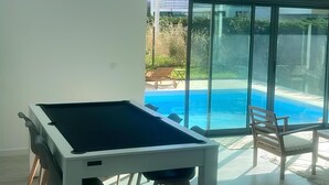 Quarto espaçoso com mesa de bilhar, grandes janelas e vista para uma piscina.
