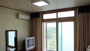 A living room with a television, a flat-screen TV, a sofa, and a sliding glass door leading to a balcony. - Il Sung Jeju Beach Resort (Jeju City)