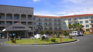 A multi-story building with a central courtyard, a large circular sculpture, and a parking area with cars. - Il Sung Jeju Beach Resort (Jeju City)