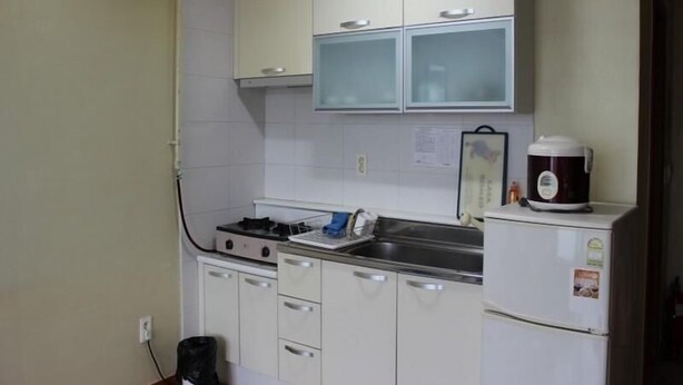 A kitchen with white cabinets, a stove, a sink, and a refrigerator. - Il Sung Jeju Beach Resort (Jeju City)