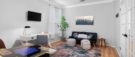A modern living room with a flat-screen TV, a ceiling fan, a gaming table, a couch, and a potted plant.