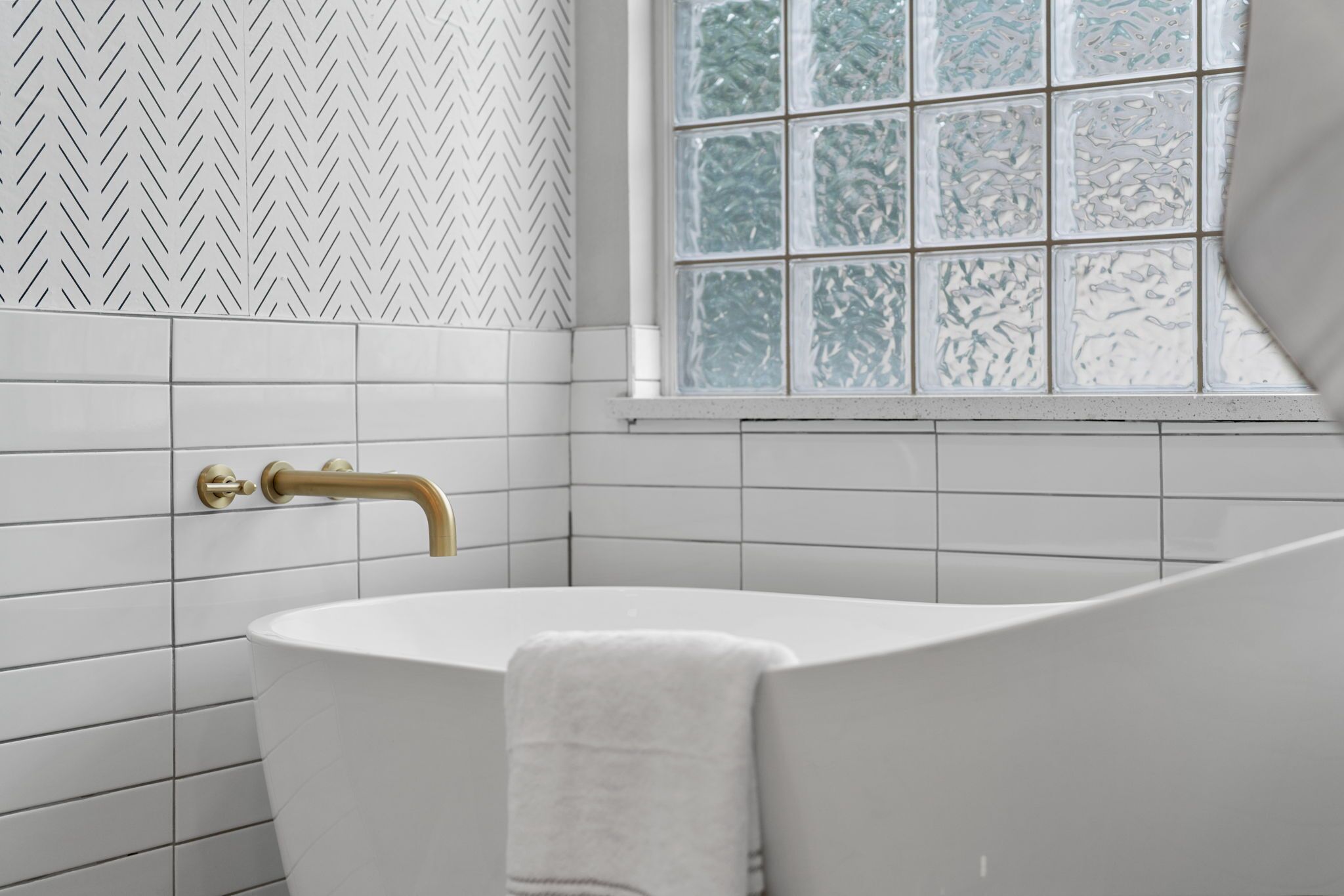 A bathroom with white tiles, a gold faucet, and a window with frosted glass.
