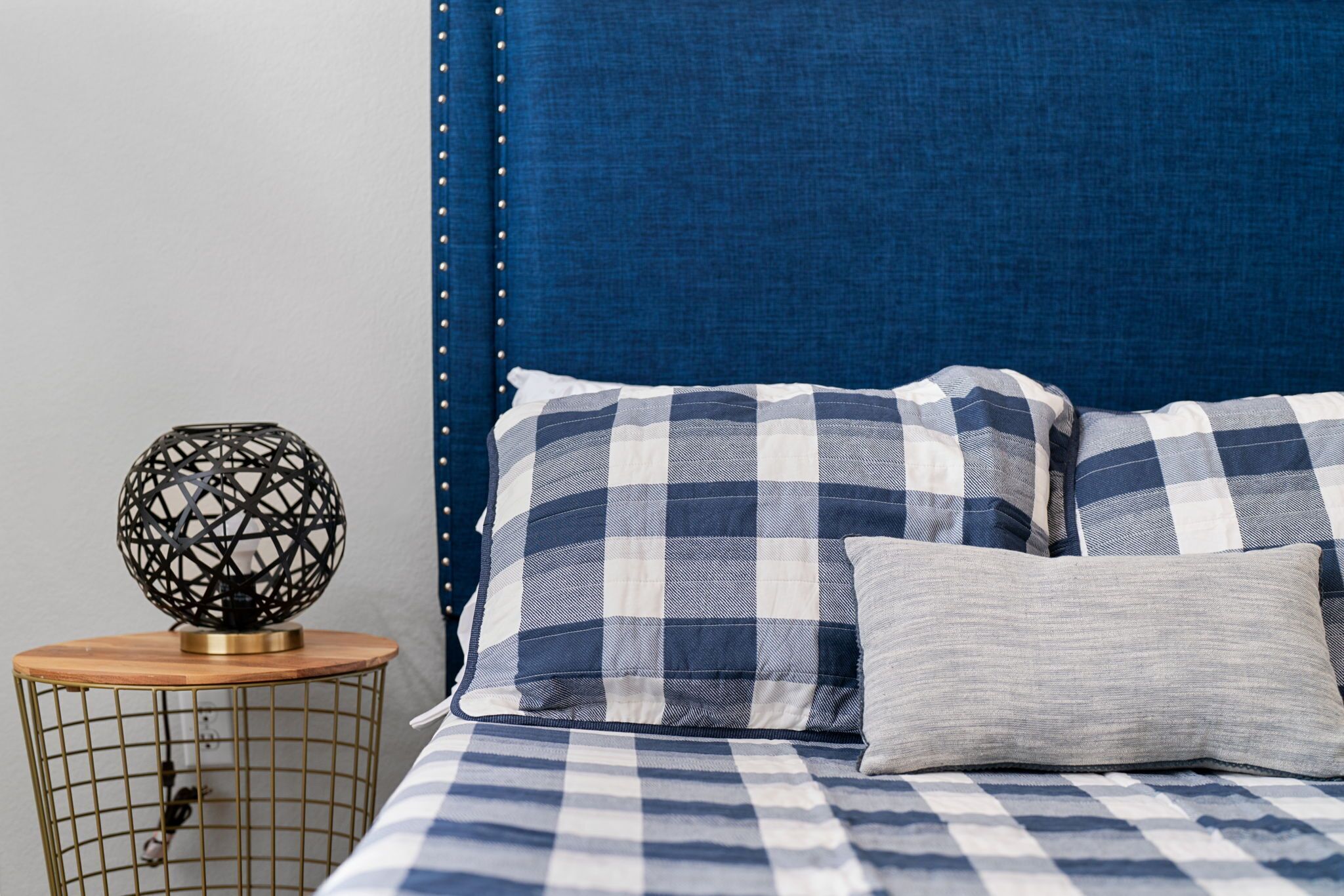 A bed with a checkered blue and white bedspread, a grey pillow, and a blue upholstered headboard.