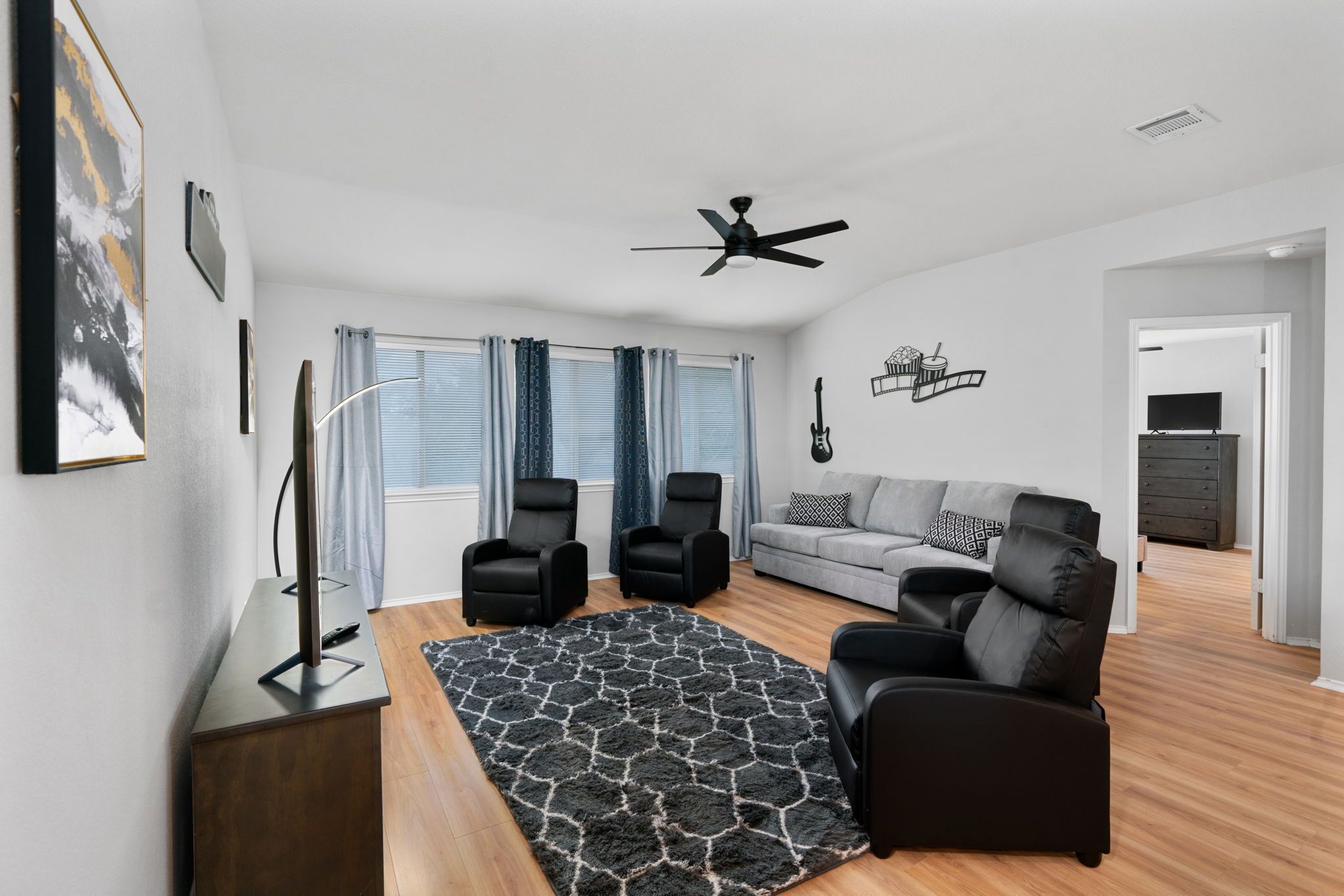 A modern living room with a sofa, two armchairs, a coffee table, a ceiling fan, and a patterned rug.