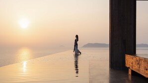 A person walking on a reflective surface near a wooden structure with a view of the water and distant landforms. - Alila Dong Ao Island Zhuhai (Zhuhai)
