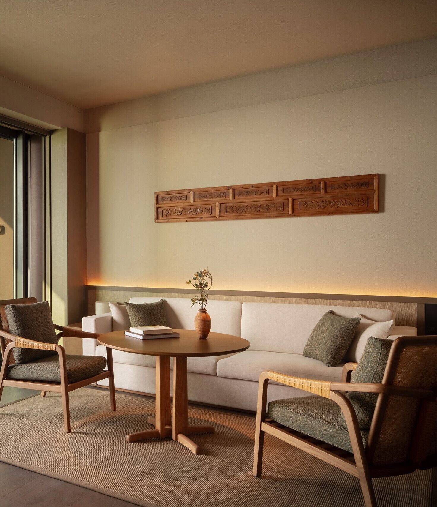 Un salon moderne comprenant un canapé, deux fauteuils, une table ronde en bois et un panneau décoratif en bois sur le mur.