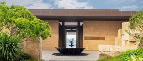 A modern building with a stone facade, a central water feature, and a pathway leading to the entrance.