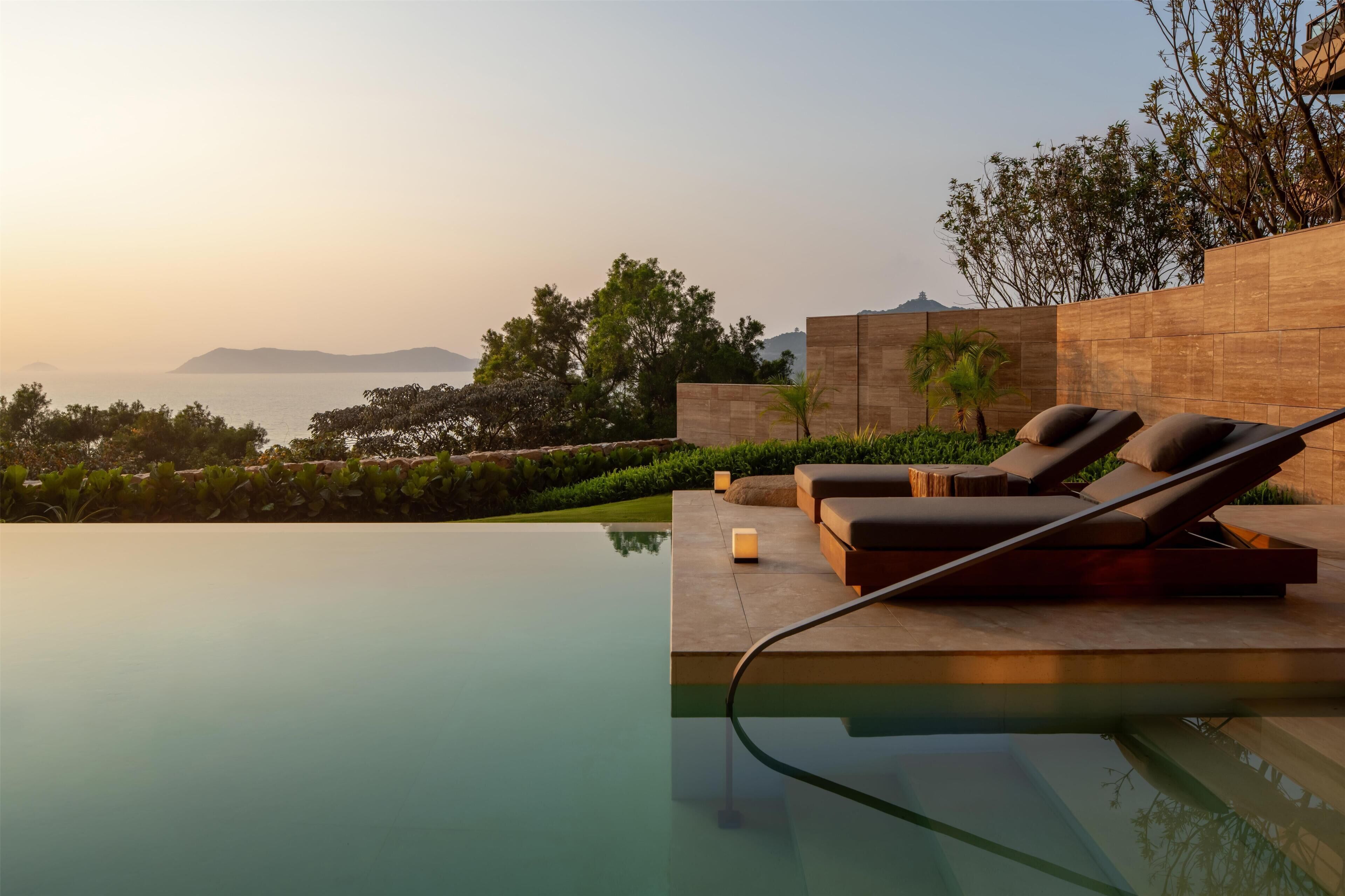 A modern infinity pool with lounge chairs and a view of the sea.