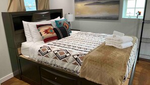 Una cama bien hecha con ropa de cama estampada, cabecera y ventana con cortinas.