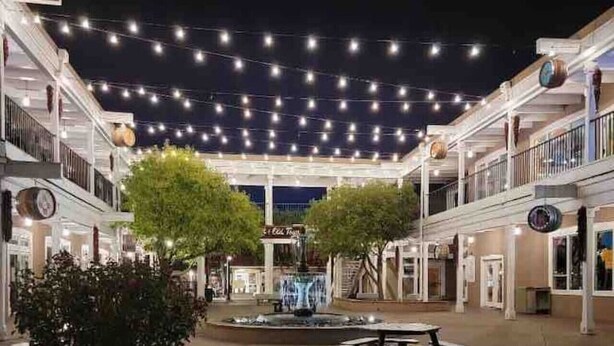Una plaza al aire libre con luces colgantes, una fuente y un espacio con asientos.