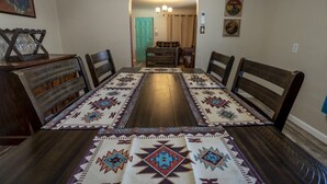 Uma sala de jantar com uma mesa de madeira comprida, quatro cadeiras e tapetes estampados.