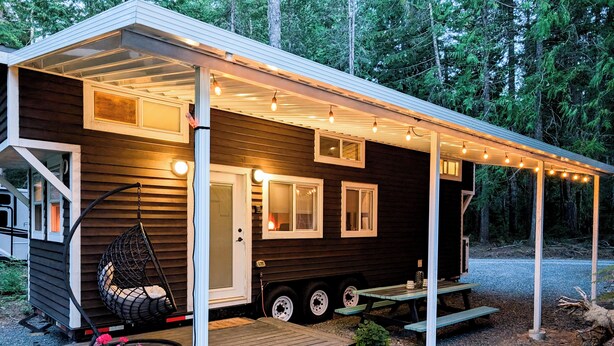 A small cabin with a porch, a hanging chair, and a table with flowers. - Cozy Tiny Home - Farm Stay - Near Qualicum Beach  (Qualicum Beach)