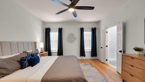 A bedroom with a bed, nightstands, a dresser, a ceiling fan, and a wall decoration. - Game Room | Near Downtown | Silos and More (Waco)