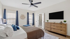 Un dormitorio con cama, ventilador de techo, cómoda y televisor montado en la pared.