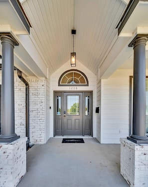 Une entrée d’immeuble avec une porte double, le numéro « 1208 » au-dessus de la porte et un paillasson noir.