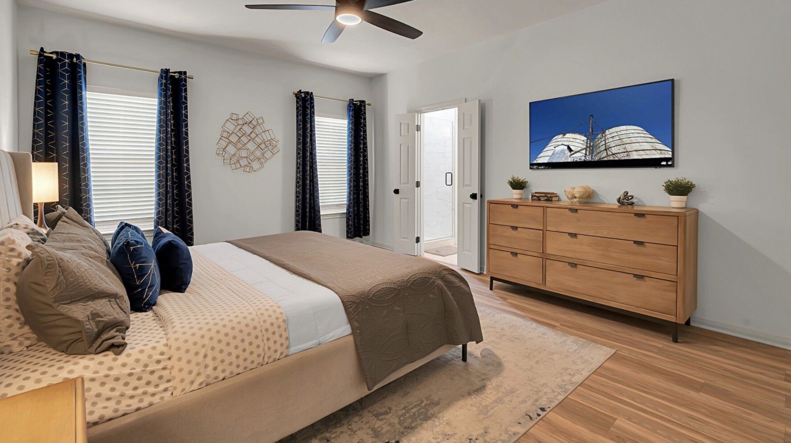 Une chambre à coucher comprenant un lit, une commode, un ventilateur de plafond et un téléviseur fixé au mur.