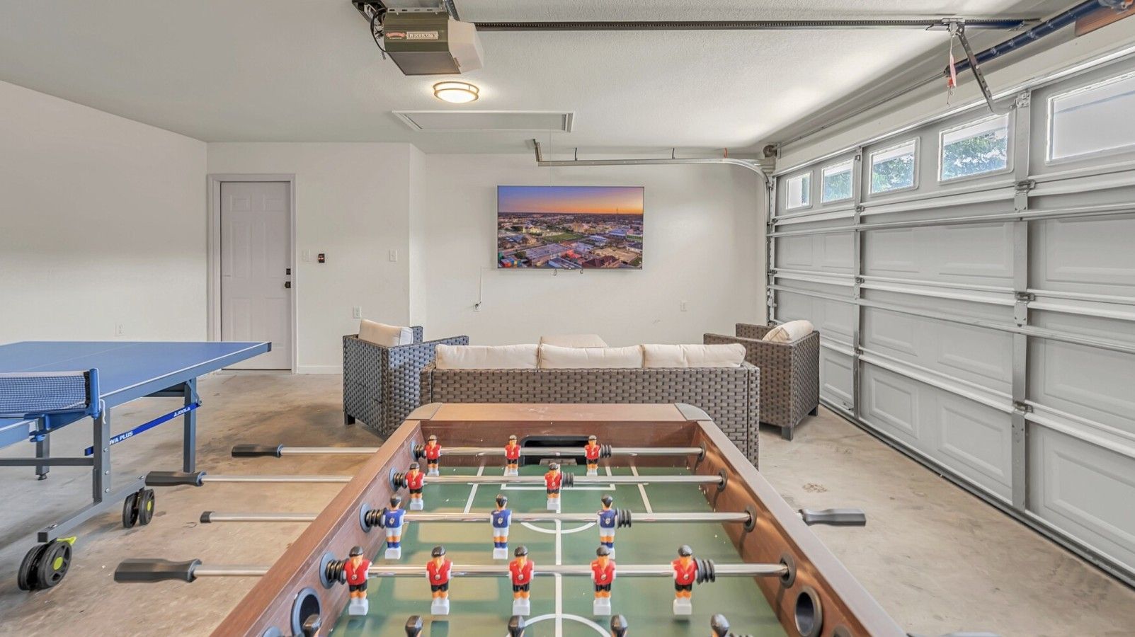 Une pièce avec une table de baby-foot, une table de ping-pong, un canapé et un tableau accroché au mur.