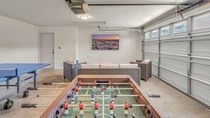 Een kamer met een tafelvoetbaltafel, een pingpongtafel, een bank en een schilderij aan de muur.
