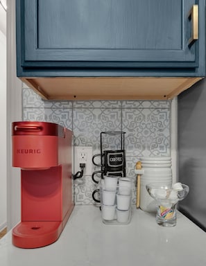 Une machine à café Keurig rouge, une autre machine à café et plusieurs tasses blanches sur un comptoir de cuisine.