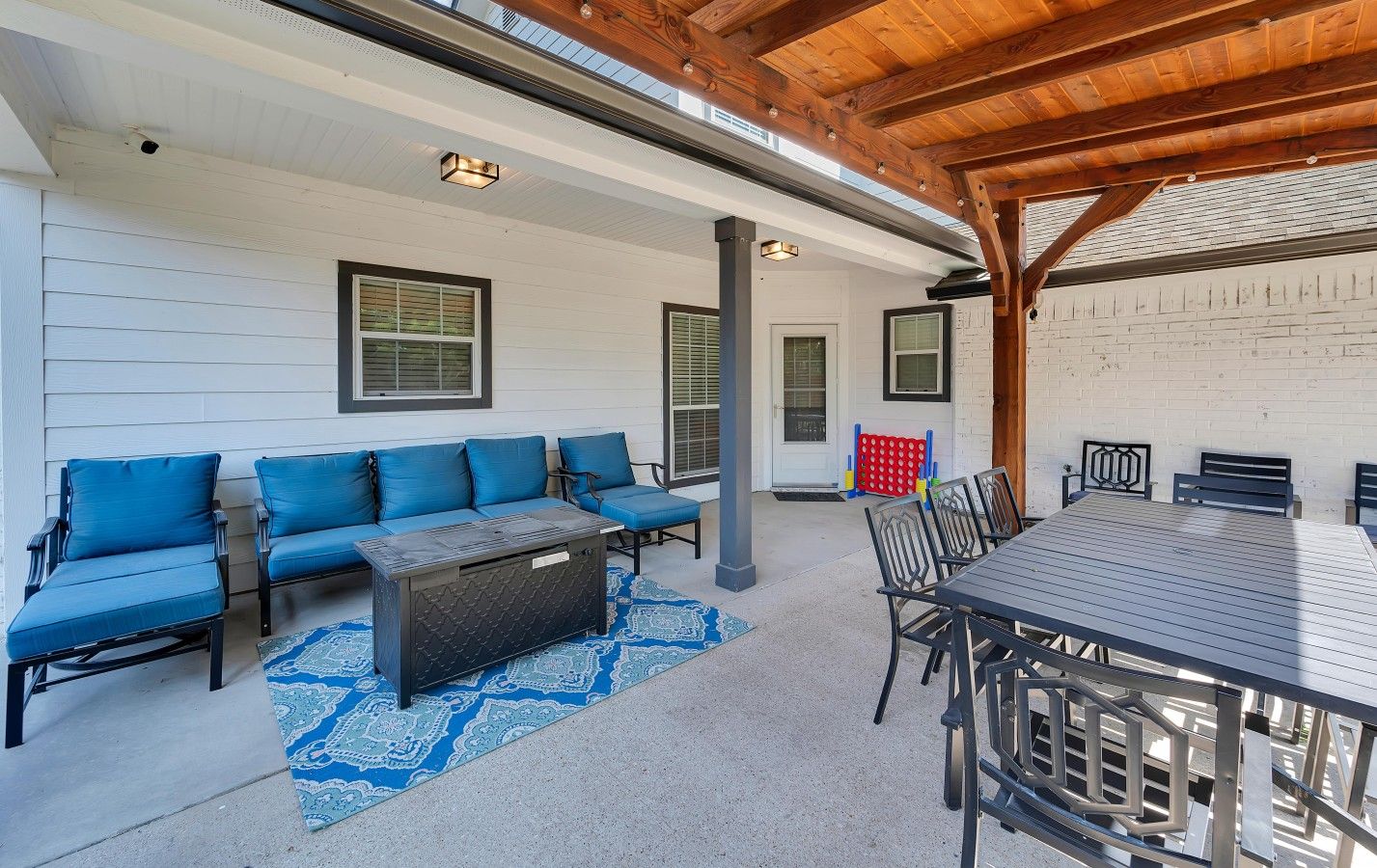 Une terrasse extérieure dotée d’un plafond en bois, d’un ensemble de canapés bleus, d’une table à manger avec des chaises et d’un tapis à motifs.