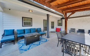 Une terrasse extérieure dotée d’un plafond en bois, d’un ensemble de canapés bleus, d’une table à manger avec des chaises et d’un tapis à motifs.