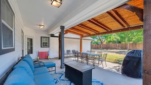 A covered patio with a dining table and chairs, a barbecue grill, and a blue outdoor sofa. - Game Room | Near Downtown | Silos and More (Waco)