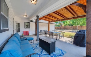 A covered patio with a dining table and chairs, a barbecue grill, and a blue outdoor sofa. - Game Room | Near Downtown | Silos and More (Waco)