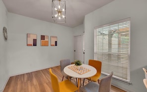 A dining area with a round table, four chairs, and a ceiling light fixture. - Game Room | Near Downtown | Silos and More (Waco)