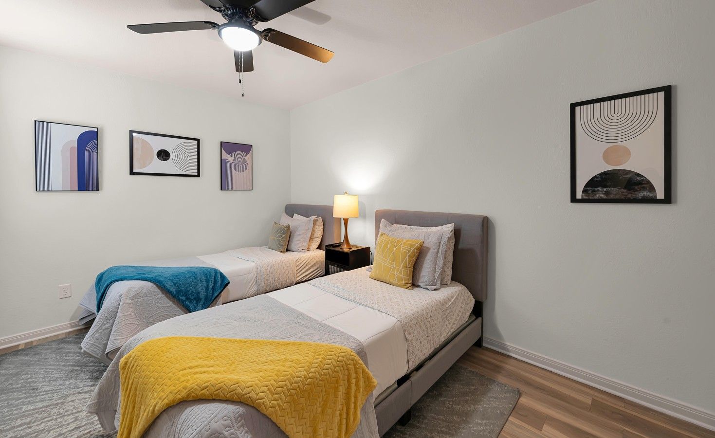 Une chambre avec deux lits, un ventilateur de plafond et des œuvres d’art murales.