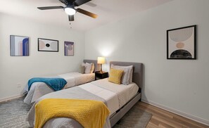 A bedroom with two beds, a ceiling fan, and wall art.